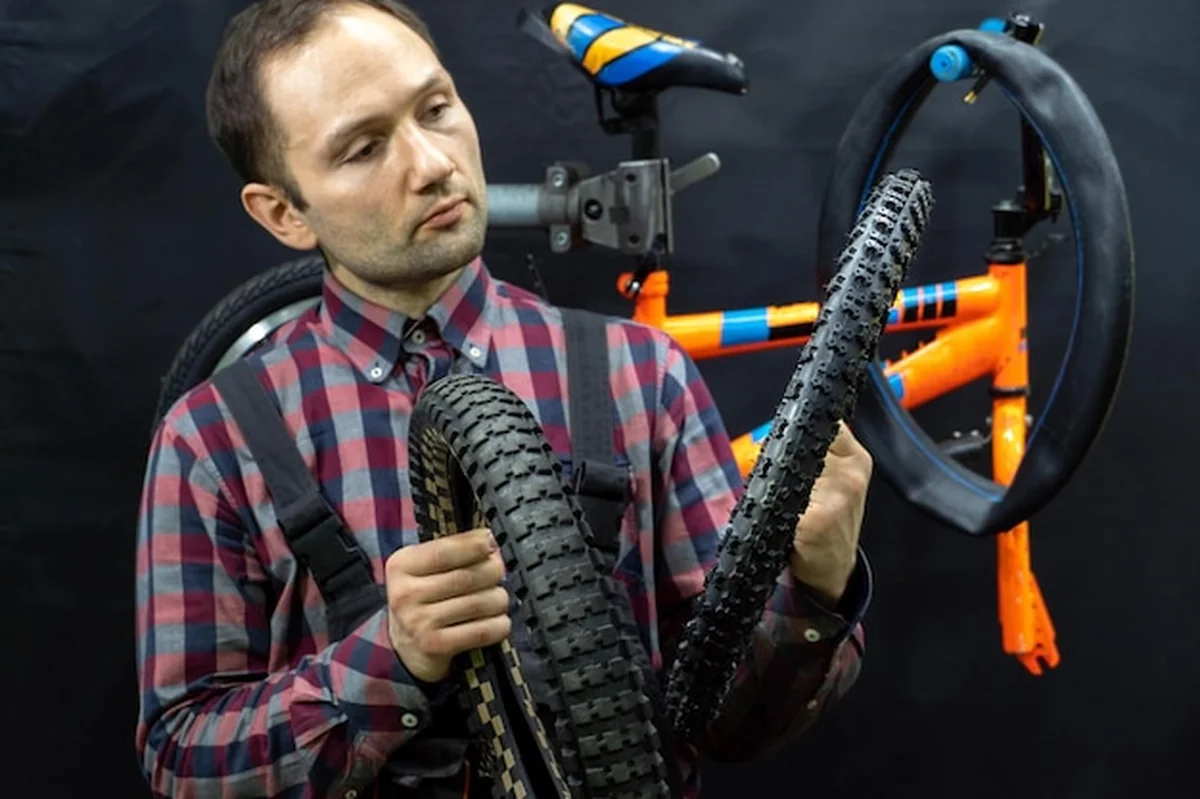 Mechanik trzymający starą pękniętą oponę w warsztacie rowerowym. Zastępowanie opony na rowerze