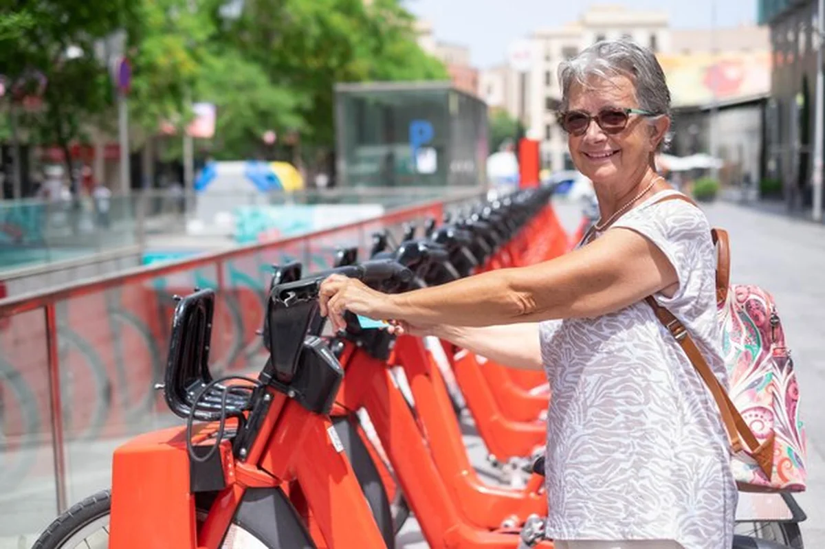 Dojrzała kobieta z siwymi włosami gotowa do wypożyczenia roweru elektrycznego, trzymająca kartę kredytową, uśmiechnięta