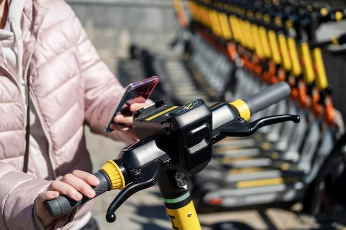 Ręce młodej dziewczyny czytają kod QR na smartfonie przy skuterach elektrycznych