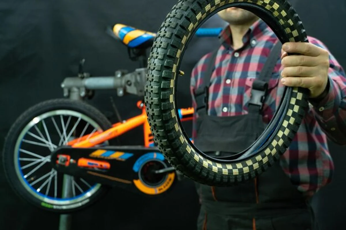 Mechanik trzyma zużytą oponę z roweru dziecięcego w warsztacie